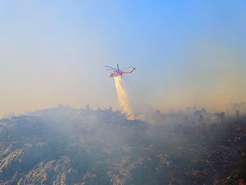 A firefighting helicopter drops water as a wildfire burns on Mount Parnitha.