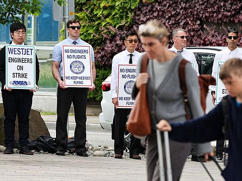 People walk with their luggage as striking aircraft maintenance engineers and technical staff represented by the Aircraft Mechanics Fraternal Association union stand in a picket line.