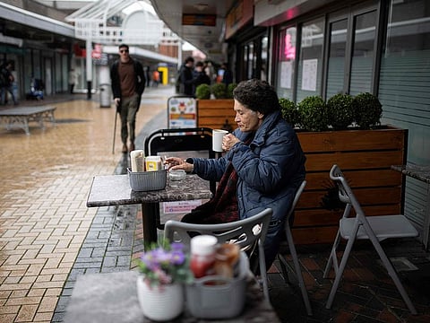 A woman enjoys a cigarette and a cup of coffee in the outdoor seating of a cafe in a pedestrianised area of the town centre of Bury, northwest England, on June 13, 2024.