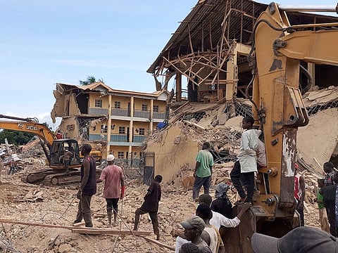 Rescue workers use heavy machinery at the site of a school that collapsed earlier in Jos, on July 12, 2024 while onlookers gather to observe the rescuing efforts.