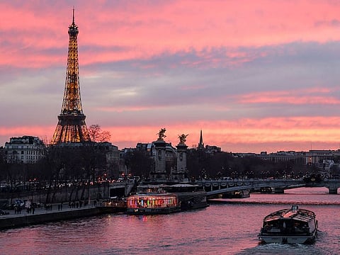 The Alexandre III Bridge and the Eiffel Tower are seen as a tourism boat cruises on the River Seine at sunset in Paris on March 16, 2023. The 2024 Paris Olympic Games are set to begin with an unprecedented open-air ceremony on the River Seine on July 26, 2024.