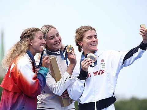 Gold medallist France's Cassandre Beaugrand (centre), silver medallist Switzerland's Julie Derron (left) and bronze medallist Britain's Beth Potter pose for a selfie after the victory ceremony for the women's individual triathlon at the Paris 2024 Olympic Games.
