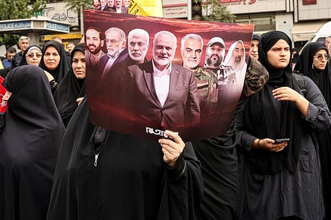 An Iranian woman holds a poster displaying (from left) Islamic Jihad secretary general Fathi Shaqaqi, Iranian physicist and scientist Mohsen Fakhrizadeh, Iraqi commander Abu Mahdi Al Muhandis, Hamas leader Ismail Haniyah, Iranian Quds Force chief Qasem Soleimani, Hezbollah commander Imad Mughnieh and Hamas spiritual guide Sheikh Ahmed Yassin, whose deaths were blamed on Israel, during the funeral procession of Haniyeh in Tehran on August 1, 2024.