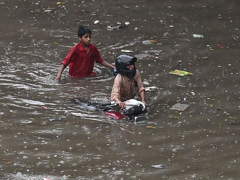 People wade through a flooded street amid heavy rainfall in Lahore on August 1, 2024.