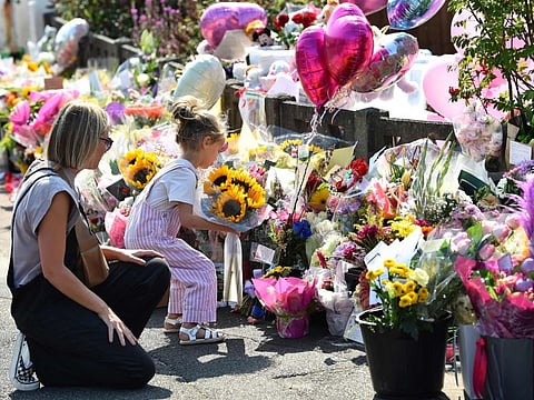 A mother looks at her child laying a bouquet of sunflowers next to floral tributes for the victims of a deadly knife attack in Southport, northwest England, on July 31, 2024.