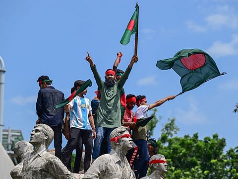 Protesters wave national flags as they stand over the Anti Terrorism Raju Memorial Sculpture during a protest in Dhaka on August 4, 2024, to demand justice for the victims arrested and killed in the recent nationwide violence during anti-quota protests.