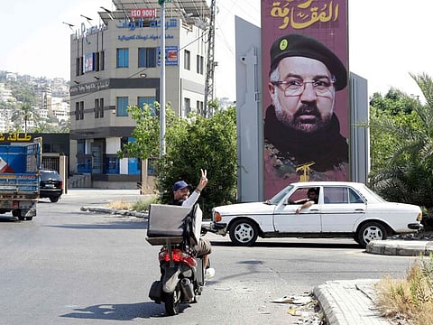 A man riding a moped flashes the V-sign for victory as he drives past a poster of assassinated Hezbollah top commander Fuad Shukr, the day after his funeral, erected along the Sidon-to-Tyre highway, in southern Lebanon.