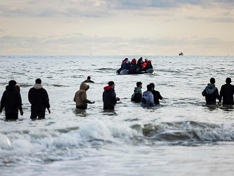 Migrants walk in the water to board a smuggler's boat on the beach of Gravelines, near Dunkirk, northern France on April 26, 2024.