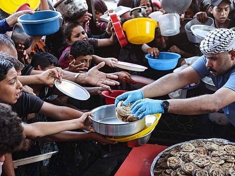 Palestinian children hold out their plates toward a man, to receive their share of vegetable patties prepared by volunteers in Beit Lahia in the northern Gaza Strip on August 14, 2024.