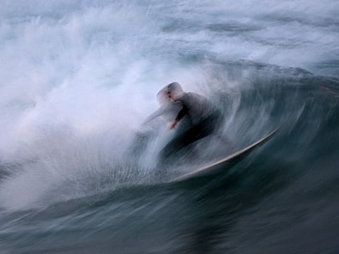 A surfer rides a wave as a rare blue supermoon lights up the sky over Bondi Beach in Sydney on August 19, 2024.