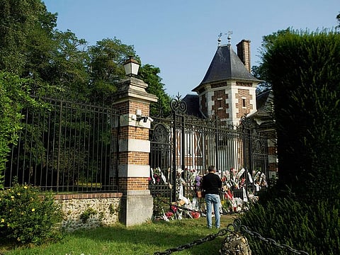 A man stands in front of the entrance of La Brulerie, the property of late French actor Alain Delon, with tribute flowers set on and next to the gate, in Douchy, central France, on August 18, 2024.