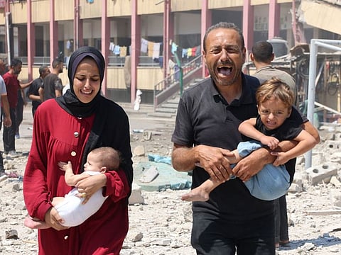 Palestinians carry their children as they flee after an Israeli strike on a school, housing displaced Palestinians, in the Rimal neighbourhood of central Gaza City on August 20, 2024.