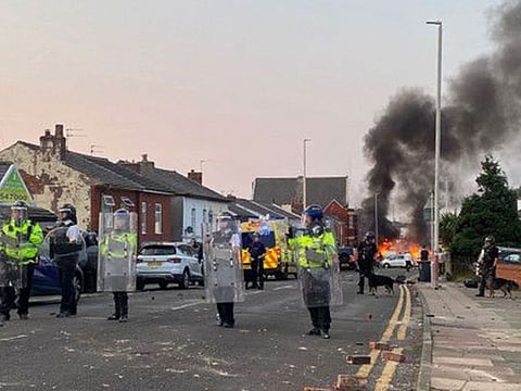 Smoke billows from a fire started by protesters as riot police stand guard after disturbances near the Southport Islamic Society Mosque in Southport, northwest England, on July 30, 2024, a day after a deadly child knife attack.