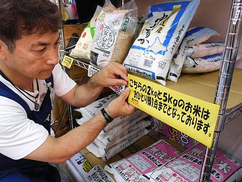 A supermarket worker putting up a sign informing customers purchasing rice to buy only one bag per person in Tokyo.