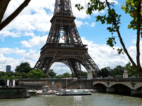 A Seine river bus boat docks in front the Eiffel Tower adorned with Olympic rings.