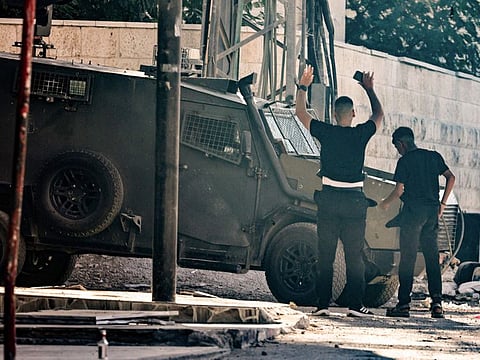 A Palestinian youth lifts his arms as he stands in front of an Israeli armoured vehicle in Jenin in the occupied West Bank on September 4, 2024.