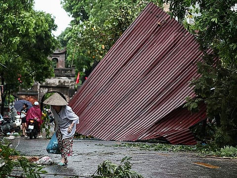 A woman walks past fallen trees and debris on a street after Super Typhoon Yagi hit Hanoi.