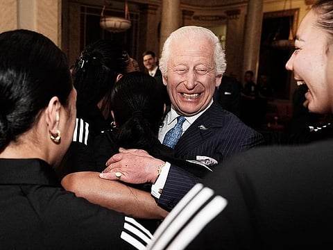 Britain's King Charles III reacts as he is hugged by members of New Zealand's Black Ferns rugby union team, at Buckingham Palace in central London on September 11, 2024.