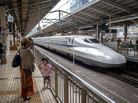 A woman taking photographs of her child in front of a high-speed train, or shinkansen, at Tokyo station in Tokyo.