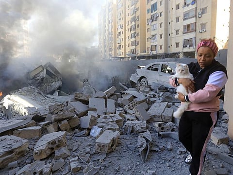 A woman carries her pet past a destroyed building at the site of an overnight Israeli airstrike in Beirut's southern suburb of Shayyah on October 2, 2024.