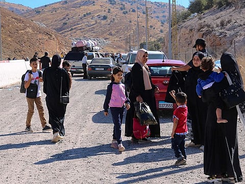 People fleeing Israeli bombardment in Lebanon, carry their belongings as they prepare to continue their journey on foot along a road damaged by an Israeli strike, in the area of Masnaa on the Lebanese side of the border crossing with Syria, on October 4, 2024.