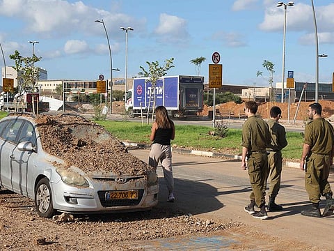 Israeli soldiers and a woman walk past a damaged vehicle in the aftermath of an Iranian missile attack on Israel, on October 2, 2024 in Tel Aviv. Israel vowed to make Iran "pay" for firing a barrage of missiles at its territory, with Tehran warning on October 2 it would launch an even bigger attack if it is targeted.