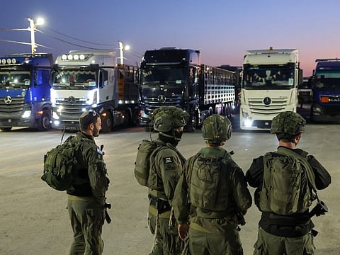 Israeli soldiers stand guard as trucks loaded with humanitarian aid delivered from Jordan wait to cross into Gaza on the border between Israel and the northern Gaza Strip, through the Israeli-controlled Erez crossing on October 21, 2024.