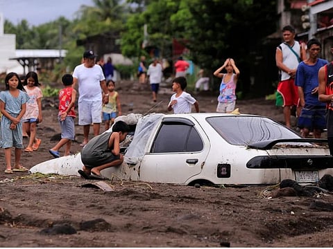 Residents look at a car buried by volcanic ash which cascaded into a village triggered by heavy rains brought about by Tropical Storm Trami at a village in Guinobatan town, Albay province south of Manila, Philippines, on October 23, 2024.