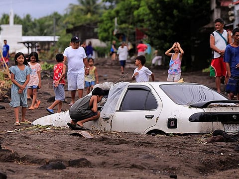 Residents look at a car buried by volcanic ash which cascaded into a village triggered by heavy rains brought about by Tropical Storm Trami at a village in Guinobatan town, Albay province South of Manila on October 23, 2024.
