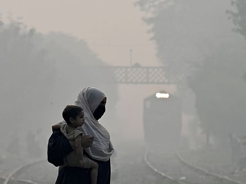 A woman carries a child as she walks across a railway track amid heavy smog in Lahore on October 29, 2024.