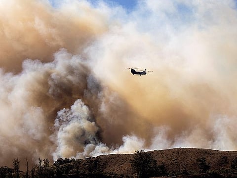 A fire helicopter flies toward the Mountain Fire’s plume as it scorches acres, the wildfire fuelled by strong Santa Ana winds, in Moorpark, California.