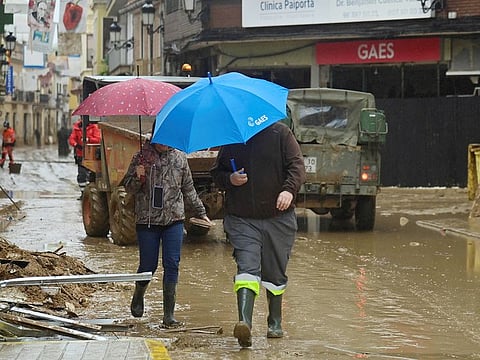Pedestrians shelter from the rain under umbrellas in a street covered in mud in Paiporta, south of Valencia, eastern Spain, on November 13, 2024 in the aftermath of deadly flooding.