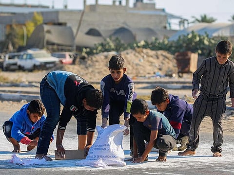 Palestinian boys scrape flour off the ground after a bag fell from an aid truck driving down the Salaheddin road in Deir Al Balah in the central Gaza Strip on November 5, 2024.