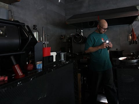 A man prepares an order using his smart phone light in the kitchen of a cafe in Tehran during electricity outage on November 12, 2024. Iran announced on November 10, 2024 that it will impose electricity rationing in Tehran and other provinces because of a shortage of fuel in power stations.
