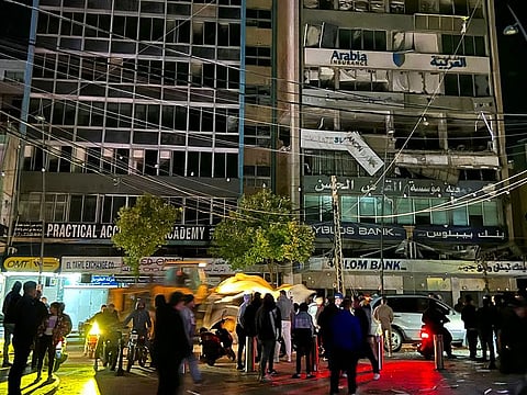 People walk at the site of an Israeli airstrike that targeted a building reportedly housing a Hezbollah backed financial institution, in the southern Lebanese city of Sidon on November 26, 2024.