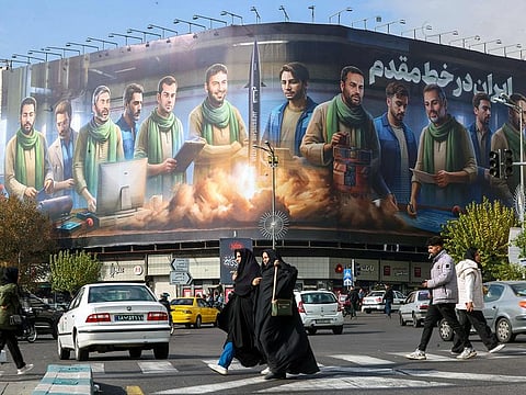 People walk past an anti-Israel billboard that reads in Farsi, "Iran on the frontline", covering the facade of a building in central Tehran.