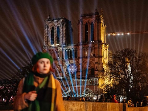 A pedestrian walks in front of the Notre-Dame de Paris cathedral illuminated in Paris on December 4, 2024, before its reopening on December 7, 2024.