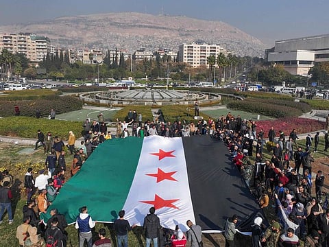 People hold a large Syrian opposition flag at Umayyad Square in Damascus on December 9, 2024.
