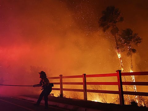 A firefighter pulls a water hose as the Franklin Fire burns palm trees near a building on December 10, 2024 on Malibu, California.