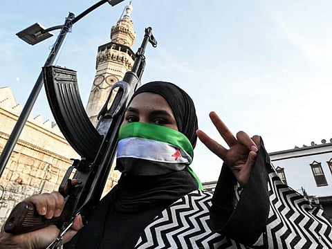 A woman masking her face with the Syrian opposition flag gestures as she holds an assault rifle outside the Umayyad Mosque in Damascus on December 10, 2024.