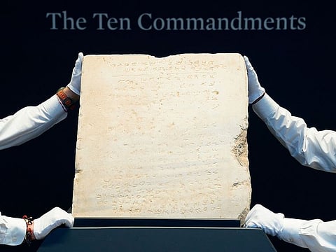 Sotheby’s workers hold one of the most widely known and influential texts in history: the oldest inscribed stone tablet of the Ten Commandments during a press preview at Sotheby’s in New York, on December 9, 2024.