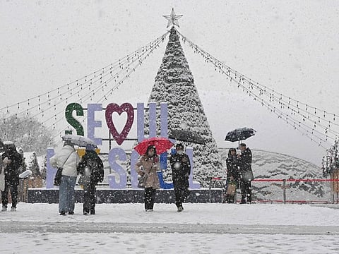 People walk in the snow at Gwanghwamun square in central Seoul on December 30, 2023.