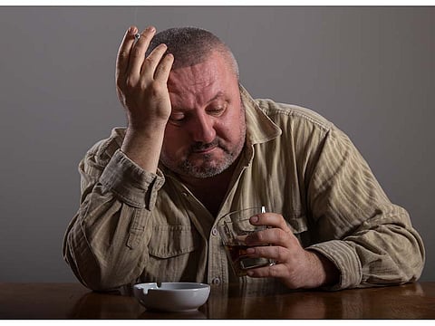 man smoking a cigarette looking on the glass with alcohol