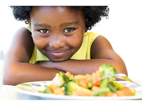 child smilng in front of vegetables