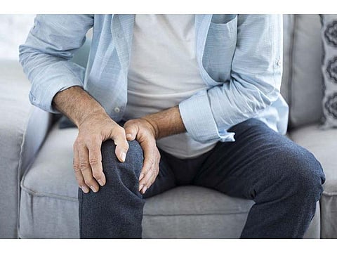 man holding his knee in pain sitting on the chair