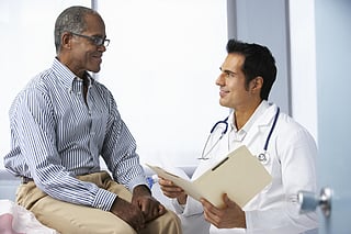 Doctor In Surgery With Male Patient Reading Notes