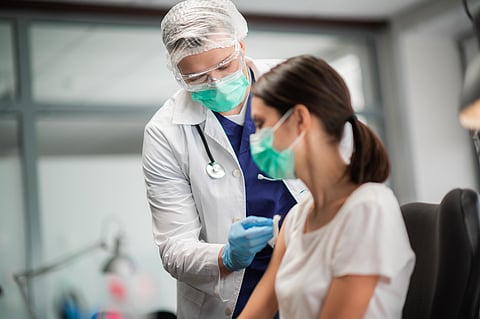A young woman in a mask decided to get vaccinated against the coronavirus during the pandemic by an experienced doctor in the laboratory