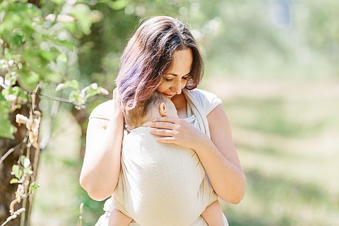 Mother carry baby girl in wrap sling in park.