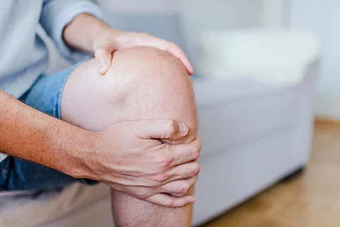 Hombre que sufre de dolor de rodilla en el sofá sentado. Un hombre maduro masajeando su rodilla dolorida. Hombre que sufre de dolor de rodilla en casa, primer plano. Dolor de rodilla