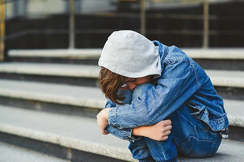 Concepto de acoso escolar. Niño sentado en la escalera, cubriéndose la cara. Triste joven colegial fuera de la escuela. Emociones negativas, depresión, estrés.